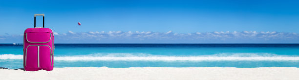 热带沙滩上的粉色手提箱。度假和旅行。长长的横幅图片下载