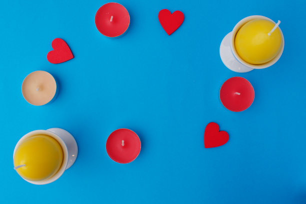 两根鸡蛋形状的黄色蜡烛放在蓝色背景上。旁边是红色的木心和小茶蜡烛。复活节卡片的概念图片下载