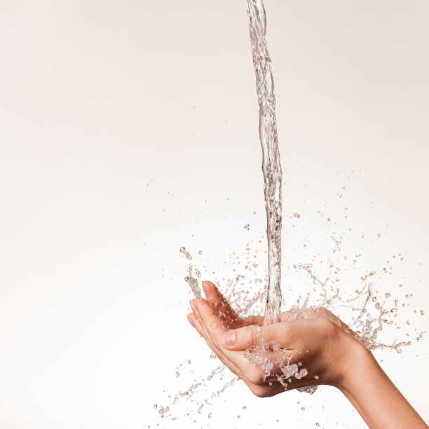 一股干净的水倾泻在女性手上的照片。人的手与下落的水和喷雾隔离白色。身体的清洁和卫生。女孩的手上有水滴。图片下载