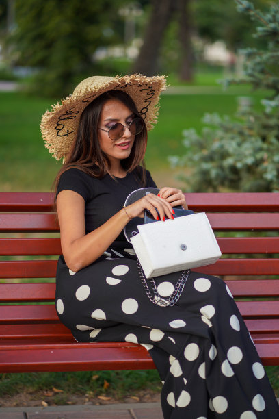 年轻女子把手机放在她的钱包，而坐在长凳上，库存照片图片下载