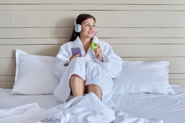 成熟的女人躺在床上，戴着耳机，拿着智能手机，戴着绿苹果图片下载