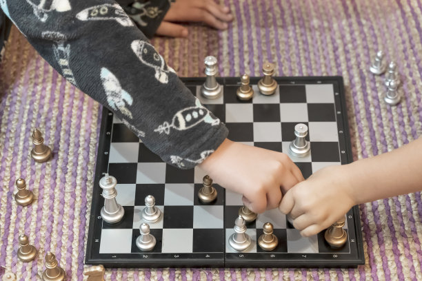 一个孩子的手和一个女孩下棋在房子的地板上的特写图片下载