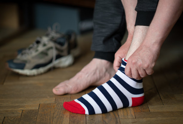 这个男人正在把彩色条纹的袜子和鞋子放在背景上图片下载