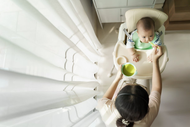 亚洲母亲喂她可爱的小男孩粥或泥在家里的高座位上。高角度视图图片下载