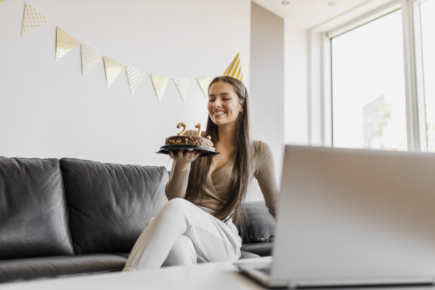 年轻女性在隔离期间在家庆祝生日，并与朋友进行视频通话。她拿着生日蛋糕图片下载