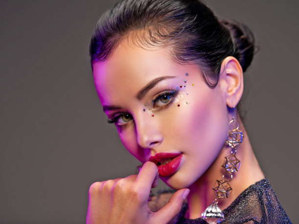 漂亮的年轻女子的肖像与明亮的化妆。闪亮的亮片。美丽的黑发与时尚的珠宝配件。一个女孩的脸在鲜艳的灯光下被突出。有耳环的女孩。图片下载