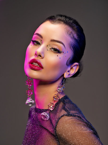 漂亮的年轻女子的肖像与明亮的化妆。闪亮的亮片。美丽的黑发与时尚的珠宝配件。一个女孩的脸在鲜艳的灯光下被突出。有耳环的女孩。图片下载