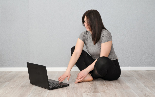 年轻漂亮的女人在室内做在线运动。呆在家里的概念。女人用笔记本电脑在线健身。图片下载