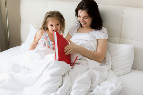 一位年轻的母亲躺在床上给孩子读书图片下载