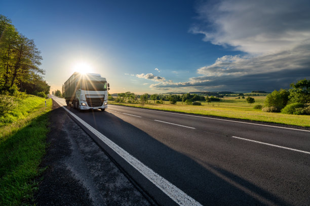 一辆白色的卡车行驶在沥青路上，在夕阳的余晖中衬托着田园风光图片下载
