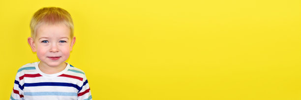 彩色背景上的快乐微笑的小男孩。黄色背景上的美丽的两岁欧洲男孩的肖像。为文本复制空间。图片下载