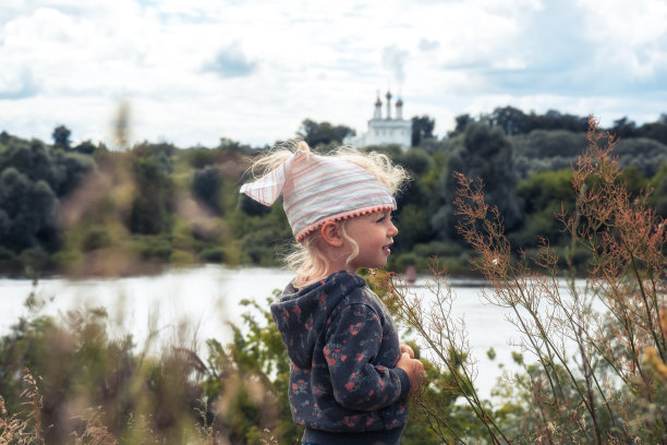快乐可爱的小女孩走在乡村田野和看着远处的河岸在暑假期间，以河流为背景的概念，快乐无忧无虑的童年生活方式图片下载