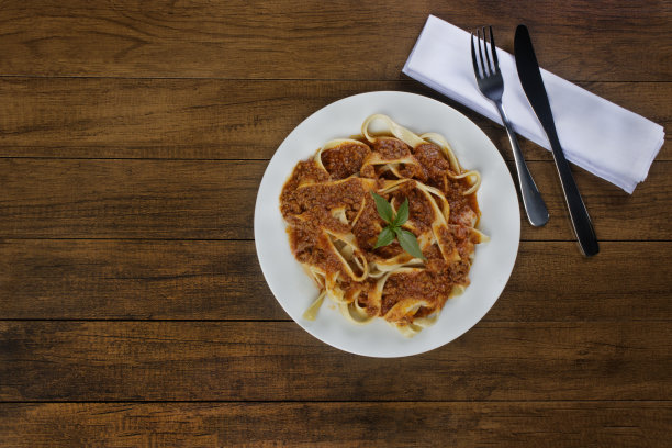 意大利扁面加肉酱和罗勒叶。餐巾纸上放刀叉。顶视图照片与自由空间的文字在左边。受欢迎的美食。图片下载