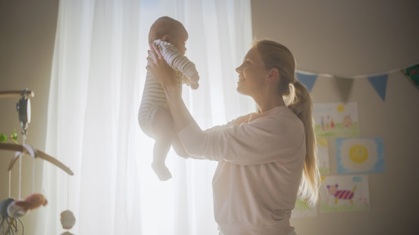 真实的照片，快乐的母亲抱着一个可爱的新生儿在舒适温暖的孩子卧室。有爱心的妈妈和刚学会走路的宝宝在家里是亲密的。童年的概念，新生活，为人父母。图片下载