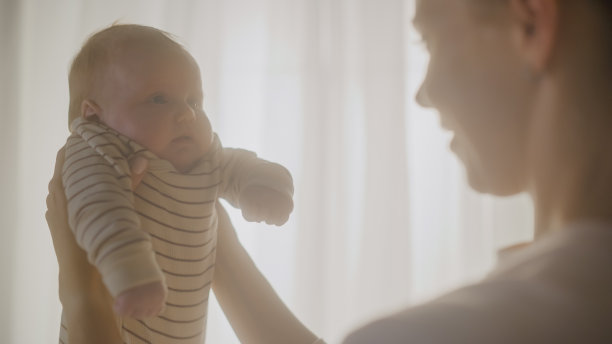 真实的照片，快乐的母亲抱着一个可爱的新生儿在舒适温暖的孩子卧室。有爱心的妈妈和刚学会走路的宝宝在家里是亲密的。童年的概念，新生活，为人父母。图片下载