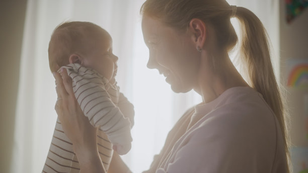 真实的照片，快乐的母亲抱着一个可爱的新生儿在舒适温暖的孩子卧室。有爱心的妈妈和刚学会走路的宝宝在家里是亲密的。童年的概念，新生活，为人父母。图片下载