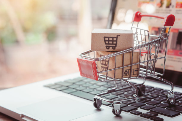 在线购物。在笔记本电脑键盘上的手推车上有一个带有购物车标志的纸板箱。网上购物服务。提供送货上门图片下载