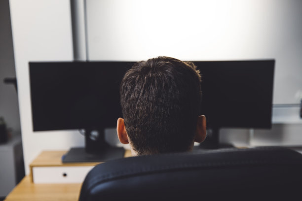 一个开发者坐在他的黑屏桌面电脑后面的后视图图片下载