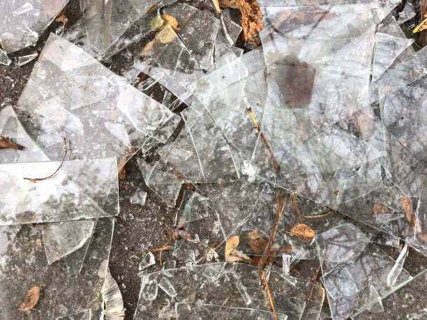 地上散落着许多尖锐的碎玻璃碎片和橙色的树叶。不同形状和大小的玻璃碎片图片下载