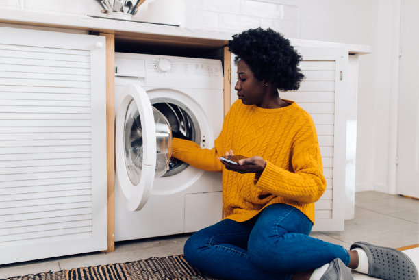 年轻女子准备她的衣服洗涤和使用智能手机图片下载