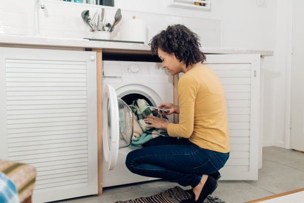 一名非裔美国妇女正在准备洗衣服并使用智能手机图片下载