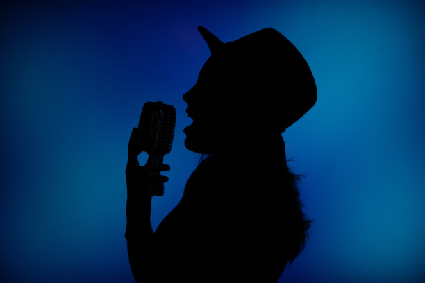 一个戴着帽子的女人的黑色剪影在蓝色的背景灯光下唱歌。图片下载