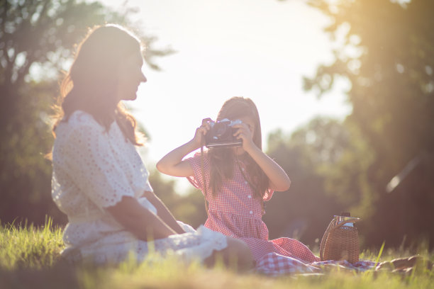 母亲和女儿坐在大自然中。小女孩给妈妈拍照片。图片下载