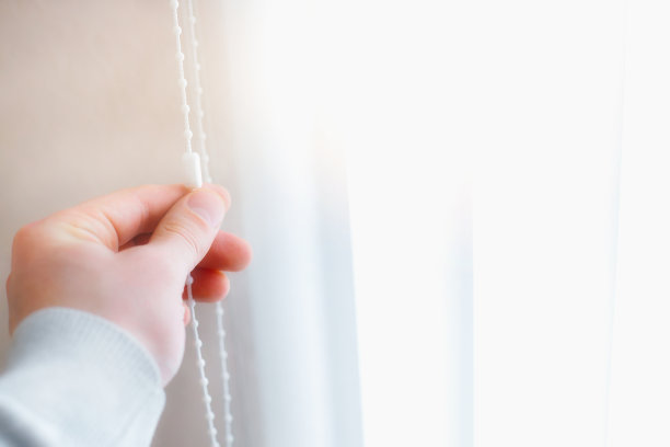 一个男人关上了窗户上的百叶窗以遮挡阳光。窗帘制造商的广告照片图片下载