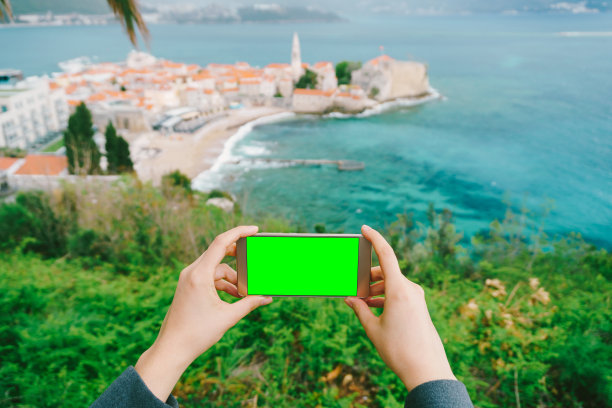 手拿着一个黑屏的智能手机。远处是一个古老的小镇。黑山共和国图片下载