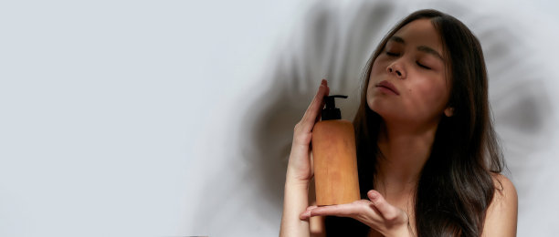 一个年轻美丽的半裸亚洲女孩的肖像长头发代表拿着一瓶护理产品闭上眼睛图片下载