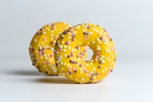 白色的巧克力甜甜甜圈，白色的背景上点缀着五颜六色的糖屑图片下载