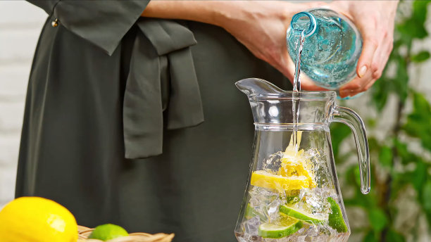 喝水。女人的手倒新鲜的纯净水与柠檬片从水壶到玻璃杯在早上的健康和饮食概念。健康的生活方式。保健美容。水合作用。图片下载