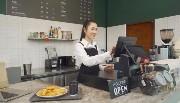 亚洲女咖啡师穿着围裙通过在线电子商务或会议销售社交媒体，咖啡厅餐厅收银员销售产品的肖像。咖啡厅服务员。人们的生活方式。图片下载
