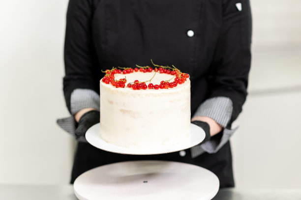 一位专业的女糕点师在厨房里准备一个甜蛋糕，并在上面放上红醋栗图片下载