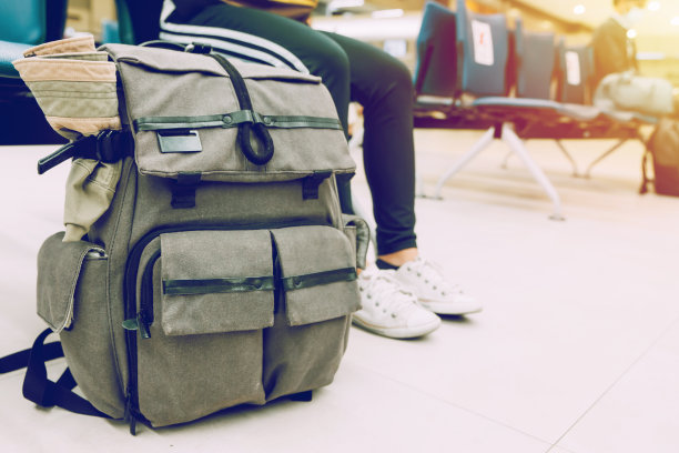 一个灰色的旅行背包放在地上，一个游客的包放在地板上，一个人坐在椅子上等待登机。日落时有光效应。图片下载