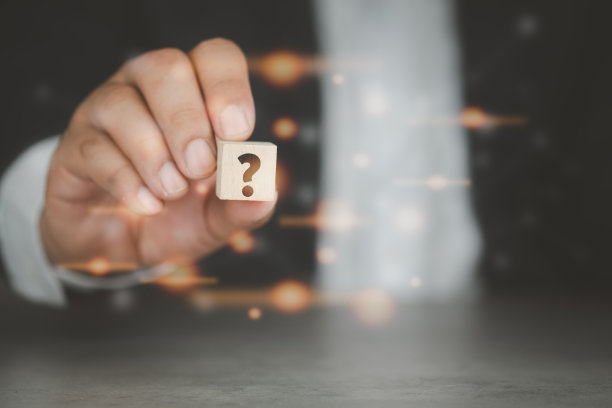 深色背景上的西装男如何在木质立方体上画上问号，模糊了橙色的光线。问题的概念。图片下载