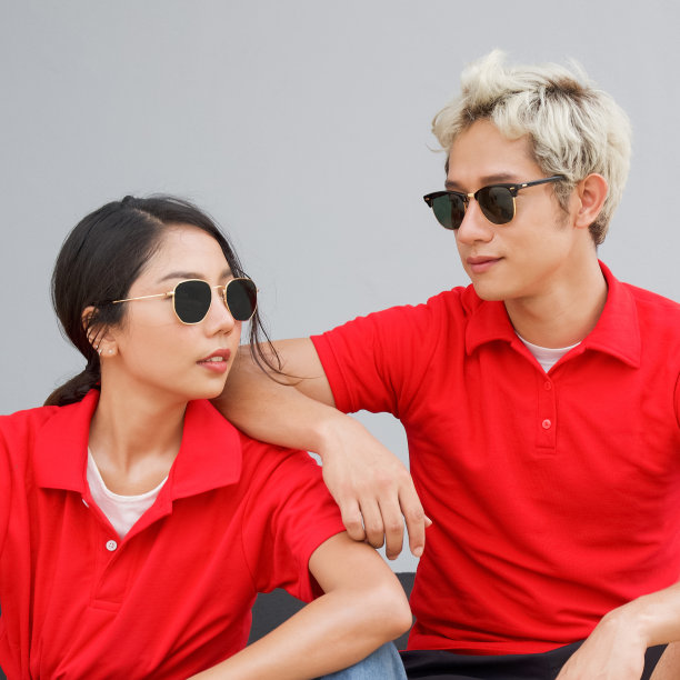 一对年轻的亚洲夫妇，穿着红色t恤，戴着黑色太阳镜，看着对方。肖像在灰色背景。图片下载