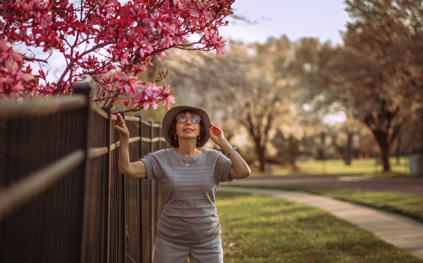 迷人的老女人享受盛开的紫木兰花在日落;图片下载