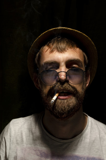 有魅力的人抽烟。一个抽着烟的嬉皮士。香烟烟雾。一个男人戴着眼镜和帽子抽烟。烟草。图片下载