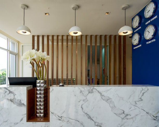 一个长长的白色大理石接待柜台位于酒店大堂。侧壁上有一个时钟，可以显示不同国家首都的时间。伦敦、纽约、曼谷和东京图片下载