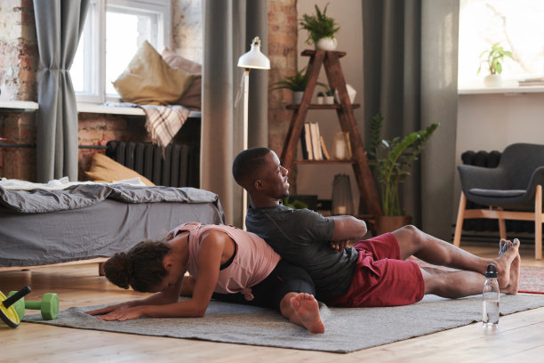 运动的年轻女子穿着舒适的衣服做伸展运动的髋关节和脊柱与她的男友的帮助图片下载