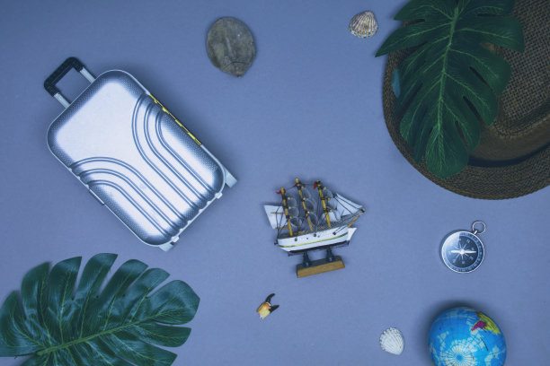 海上旅行的概念。一个带帽子的旅游休闲旅行箱，一艘有帆的船，背景是贝壳和指南针。图片下载