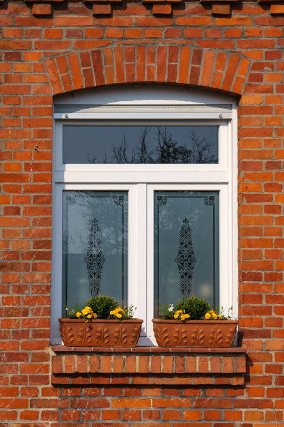带白色窗户的砖墙的碎片。窗台上有两个花盒子，上面放着黄色的花。图片下载