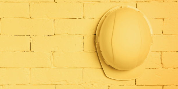 一个黄色的建筑头盔挂在砖墙上。工作场所健康和安全概念。图片下载