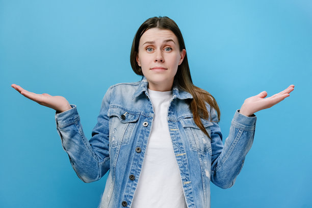 愤愤不平、困惑烦恼的年轻千禧女举手，愤怒地询问失败的原因，穿着牛仔夹克，孤立在蓝色的工作室背景。情感和误解概念。图片下载