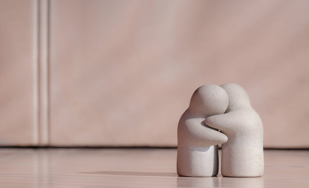 迷你花园观赏性人玩偶在拥抱姿态瓷砖地板与模糊的粉红色墙壁背景在关怀，爱和鼓励的概念图片下载