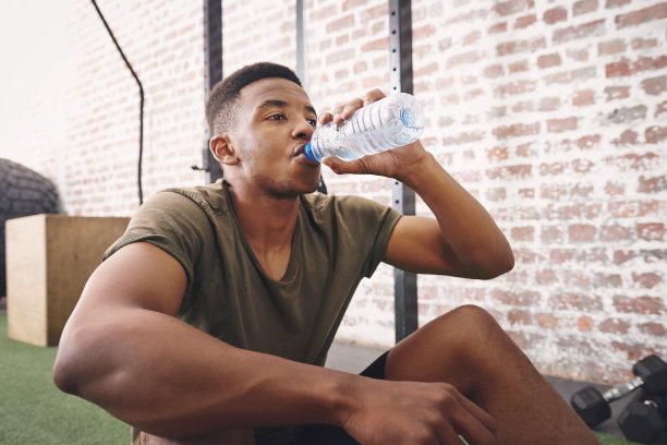 一个运动的年轻人在健身房喝一瓶水的照片图片下载