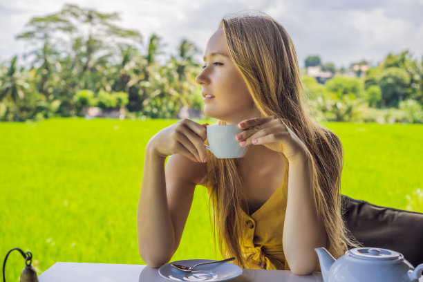 在印度尼西亚巴厘岛的稻田附近，咖啡馆阳台上端着一杯茶的女人图片下载