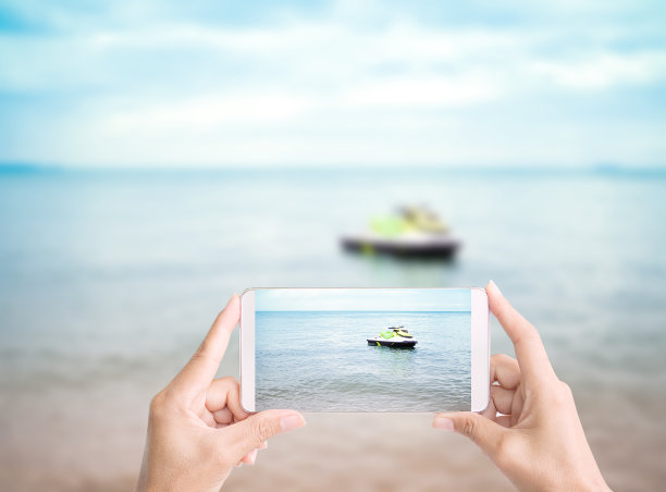 手握移动摄影师海和快艇在海岸上模糊的蓝色海洋和蓝天度假放松。科技智能手机照片旅游热带假期夏季自然概念图片下载