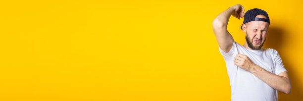 年轻人戴着帽子和t恤，腋窝汗臭，黄色背景图片下载